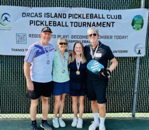four pickleball players stand in front of tournament banner wearing medals